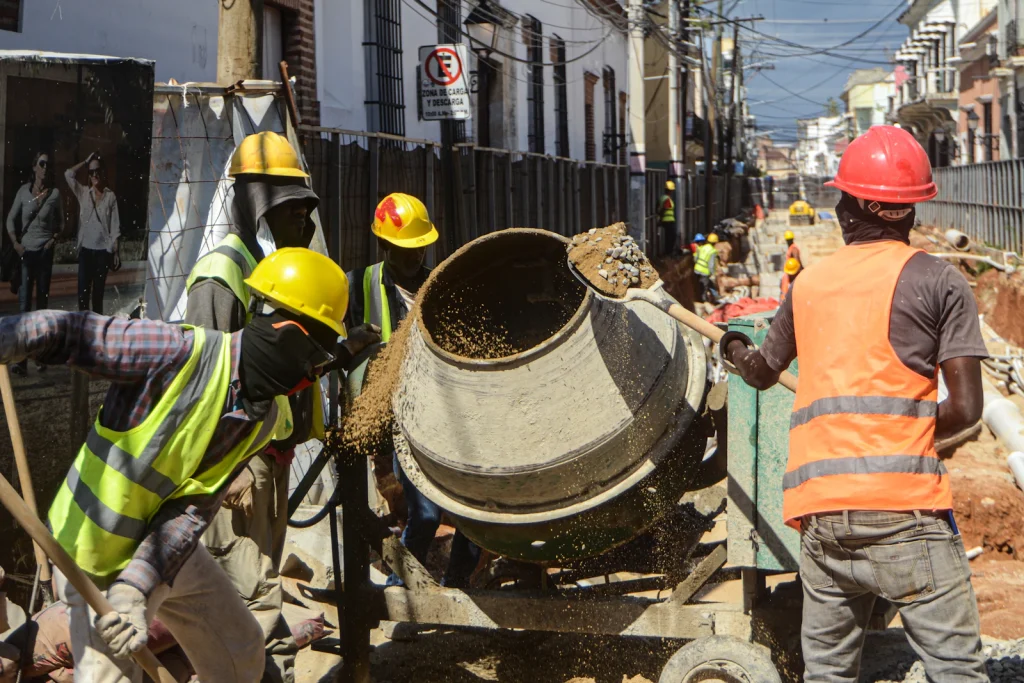 Construction crew in hi-vis and safety helmets working with a cement mixer on site