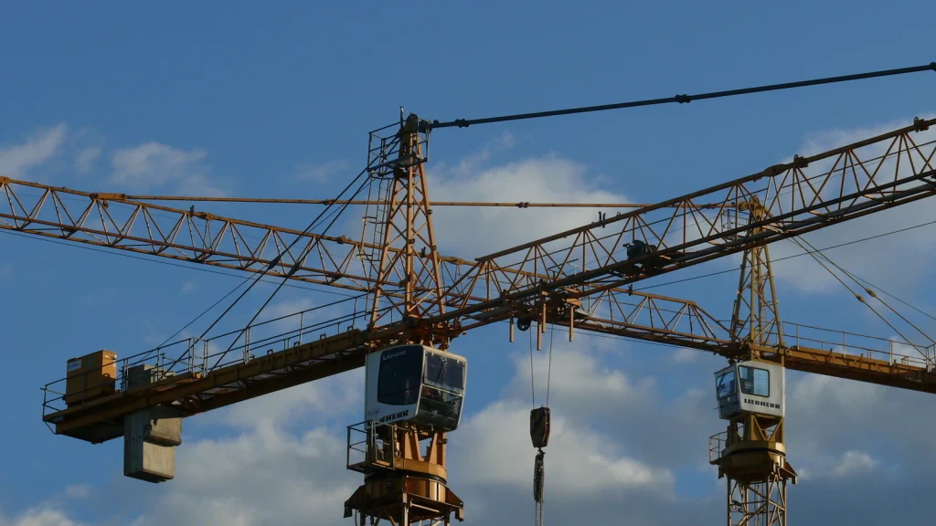 Two tower cranes with lifting hooks working above a construction site